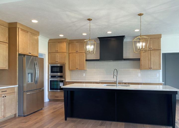 Maple kitchen with gray glass subway tile backsplash, black island and hickory hardwood floor