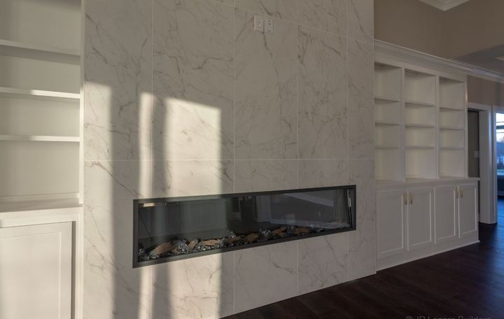 Floor-to-ceiling marble-look tile wall with linear fireplace and built-in bookcases