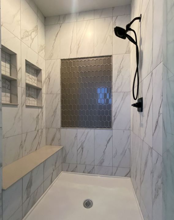 Walk-in shower with marble-look walls, bronze hexagon mosaic feature panel, bench seat and dual niches