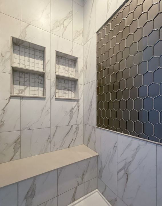 Marble-look tile shower with gray elongated hex accent wall, dual niches and quartz bench