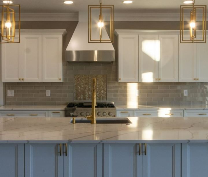 Kitchen with taupe subway tile backsplash, herringbone accent over the range and brushed gold faucet