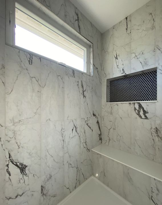 Shower with dramatic marble-look wall tile, black hex mosaic niche and quartz bench shelf