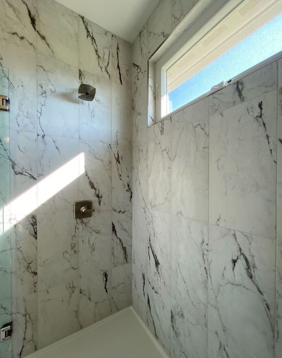 Walk-in shower with dramatic large-format marble-look tile walls and frosted transom window