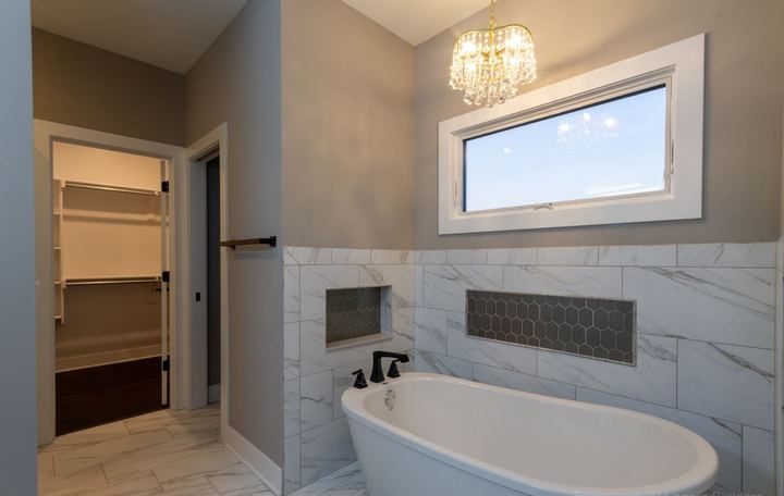 Freestanding tub against marble-look tile wainscot with hexagon mosaic niches and crystal chandelier