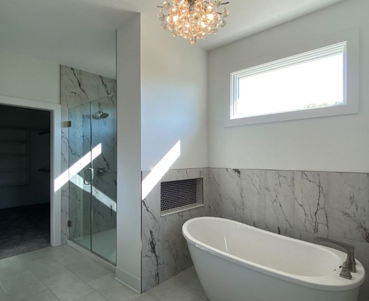 Master bath with marble-look tile wainscot, freestanding tub, penny tile niche and glass shower