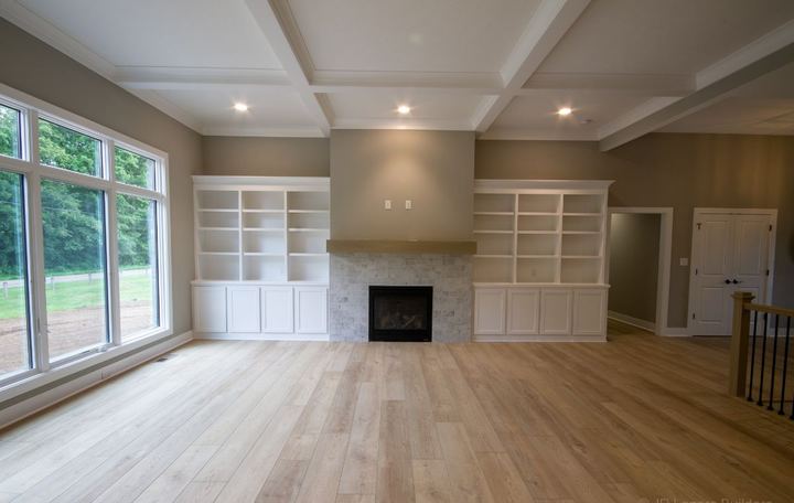 Family room with light oak wide plank flooring, whitewashed brick fireplace and built-in shelving