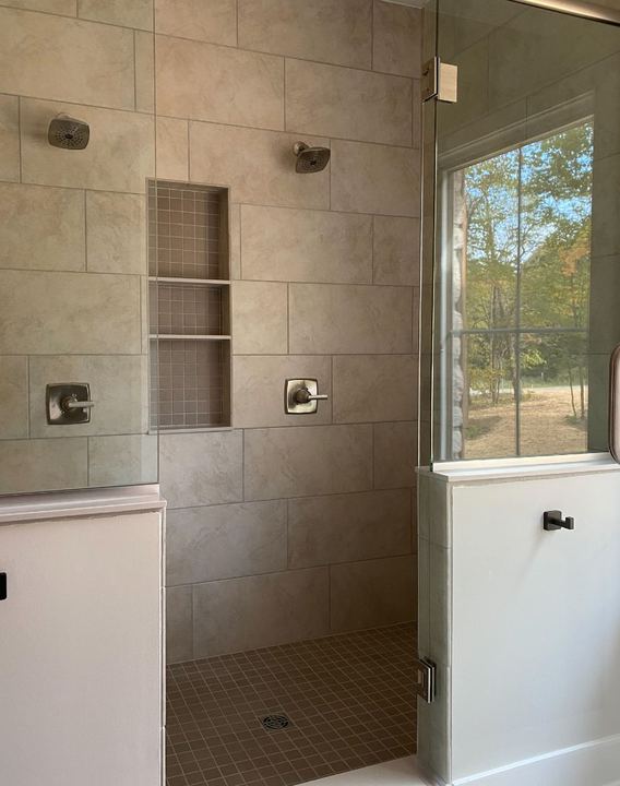 Walk-in shower with beige large-format tile, triple stacked niche, mosaic floor and frameless glass door
