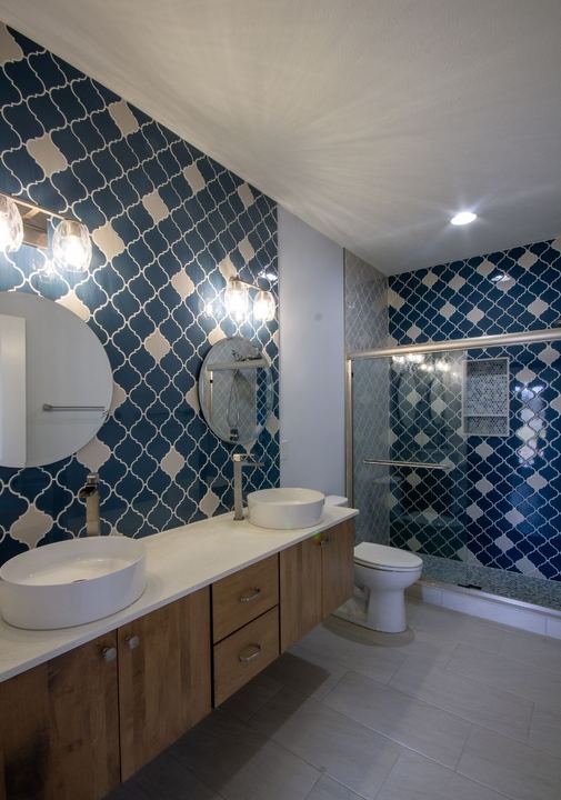 Hall bathroom with navy and white arabesque tile feature wall, floating wood vanity and vessel sinks