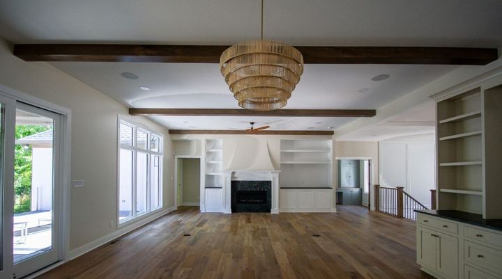 Wide-plank engineered hardwood in a great room with wood beams, built-ins and marble fireplace