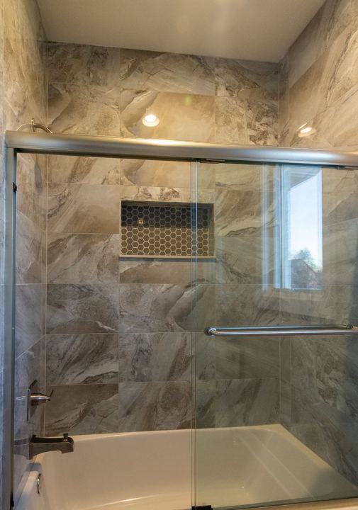 Tub and shower surround in large-format stone-look tile with hex mosaic niche and glass doors