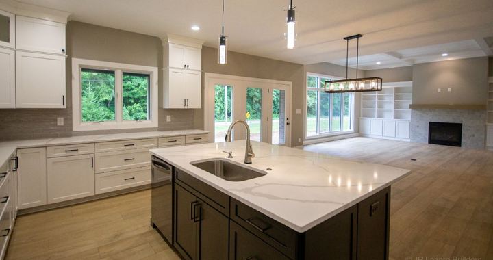 Open kitchen with marbled quartz island, taupe subway backsplash and wood-look flooring into the living room
