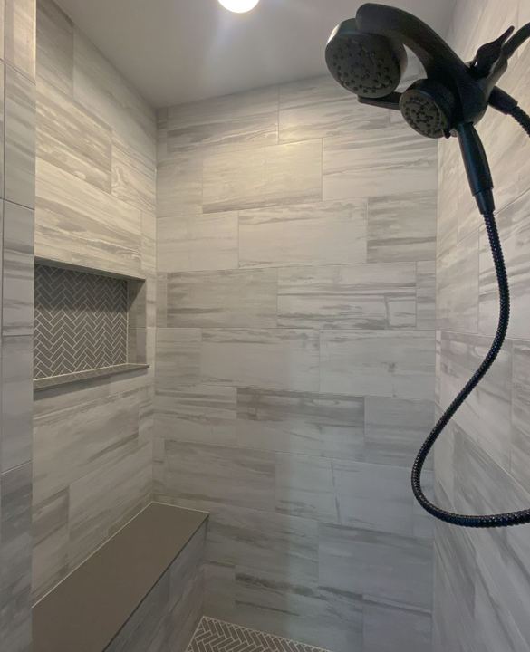 Walk-in shower with gray stone-look tile, herringbone mosaic niche and floor, bench and black dual shower head