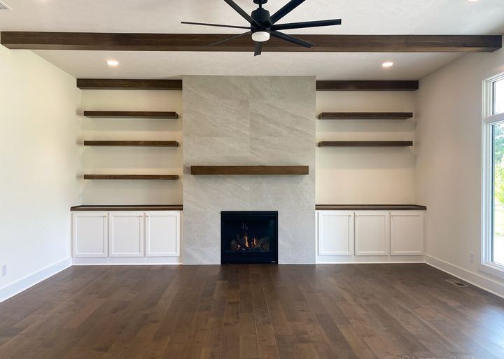 Great room with wide-plank dark hardwood floors, stone-look tile fireplace wall and floating shelves
