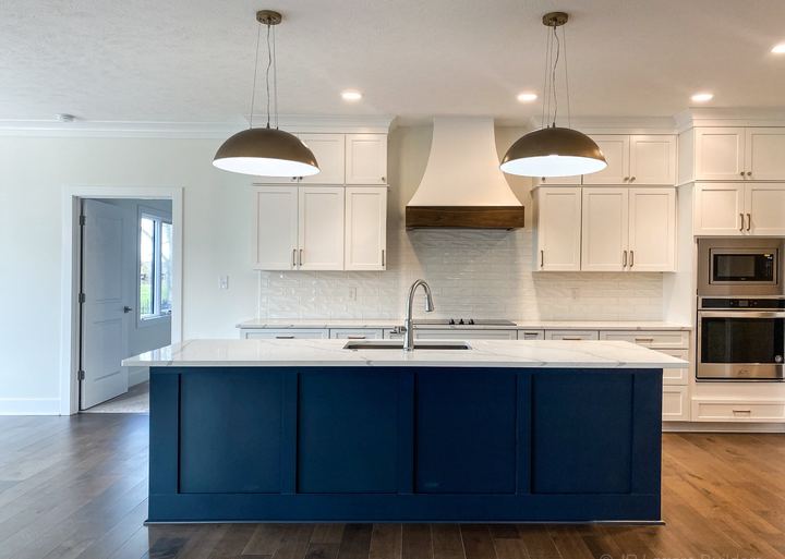 White kitchen with glossy subway backsplash, navy blue island, brass pendants and maple hardwood floors