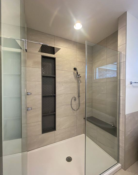 Glass walk-in shower with taupe large-format tile, stacked hex mosaic niches, rain head and hand shower
