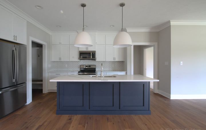 White kitchen with herringbone tile backsplash, navy blue island and hickory hardwood flooring