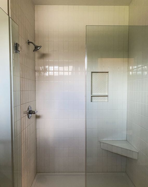 Walk-in shower with white vertical-stacked tile, herringbone niche and corner bench
