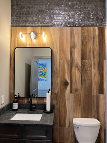 Powder room with wood-look plank tile accent wall, glossy mosaic band above and black granite vanity top