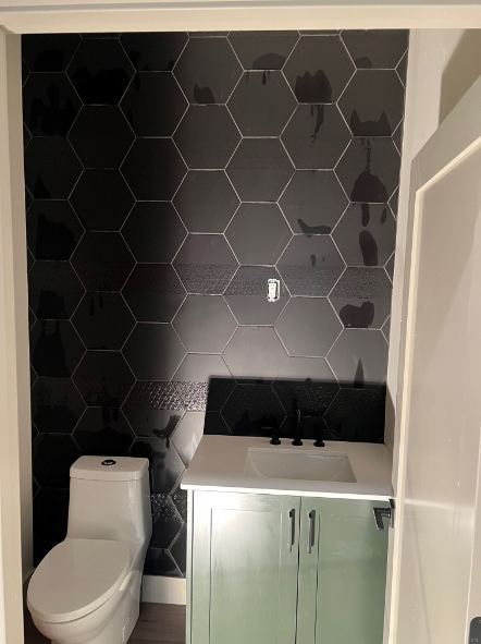 Powder room with oversized black hexagon tile accent wall behind a sage green vanity