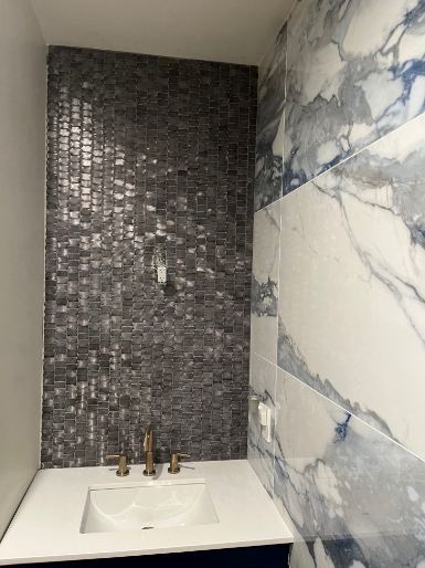 Powder room vanity with gray glass mosaic accent wall, blue-veined marble tile and gold faucet