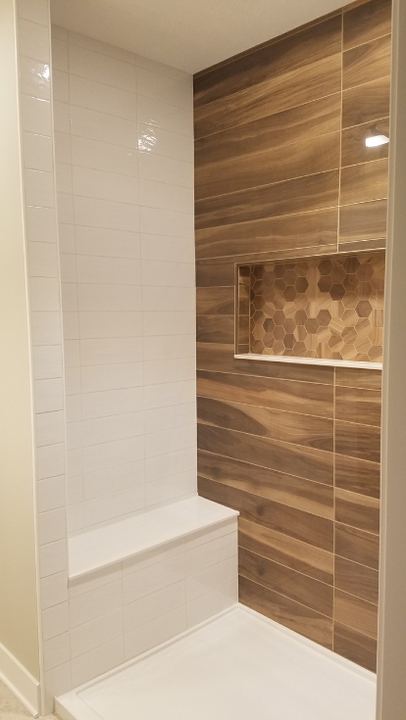 Walk-in shower with wood-look plank tile accent wall, hex mosaic niche, white subway walls and bench