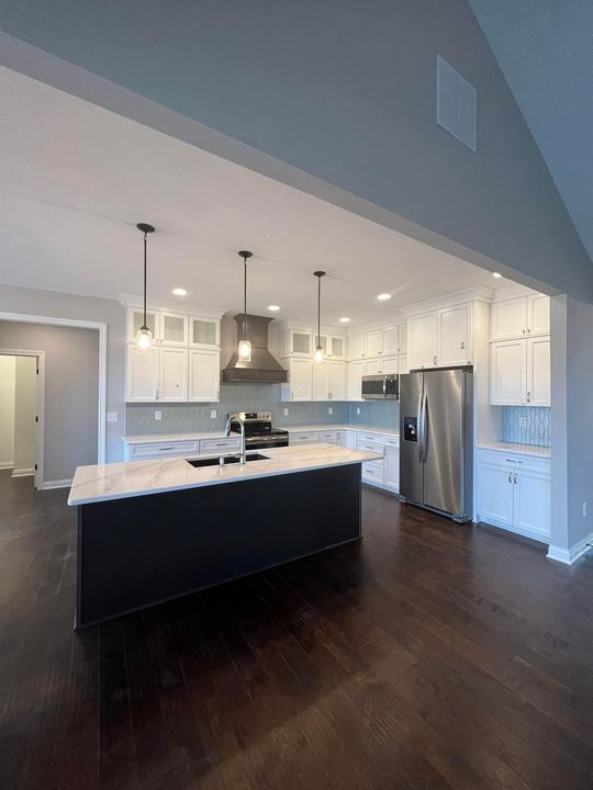 Kitchen with white cabinets, navy island, marbled quartz counters, blue glass tile backsplash and dark hardwood floor