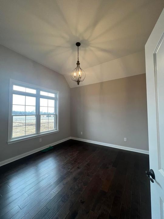 Espresso-stained hardwood flooring in a vaulted bedroom with chandelier and large windows