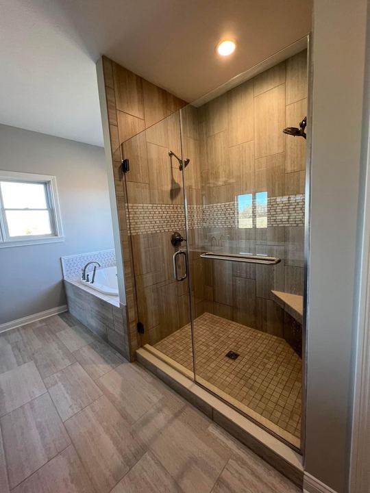 Walk-in shower with travertine-look tile, glass mosaic accent band, mosaic floor and frameless glass door