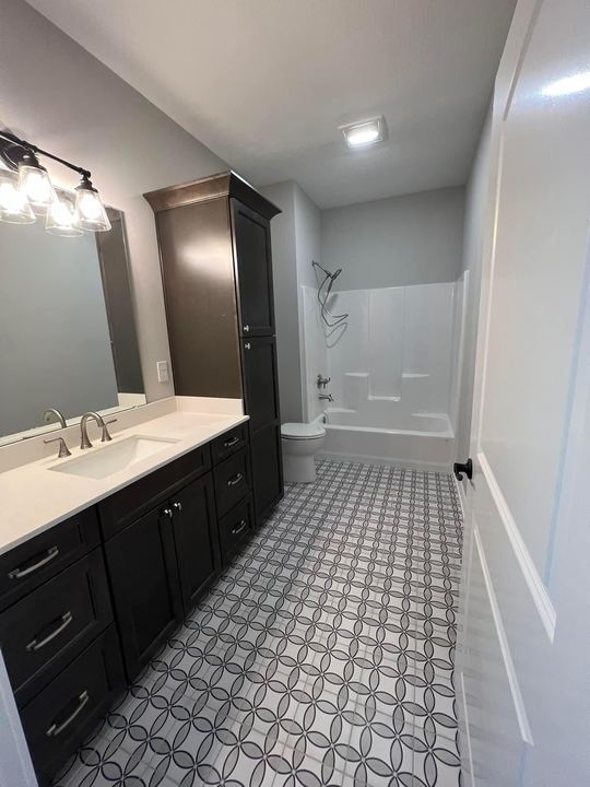 Full bathroom with gray interlocking-circle pattern tile floor, espresso vanity and linen tower