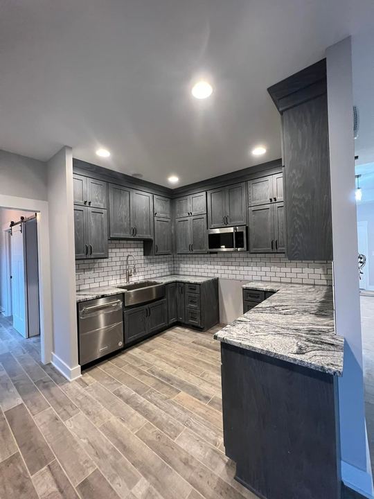 Gray shaker kitchen with white subway backsplash, granite counters and wood-look plank tile floor