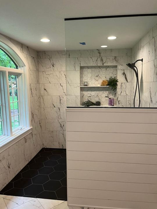 Custom walk-in shower with marble-look walls, black hexagon tile floor, hex mosaic niche and arched window