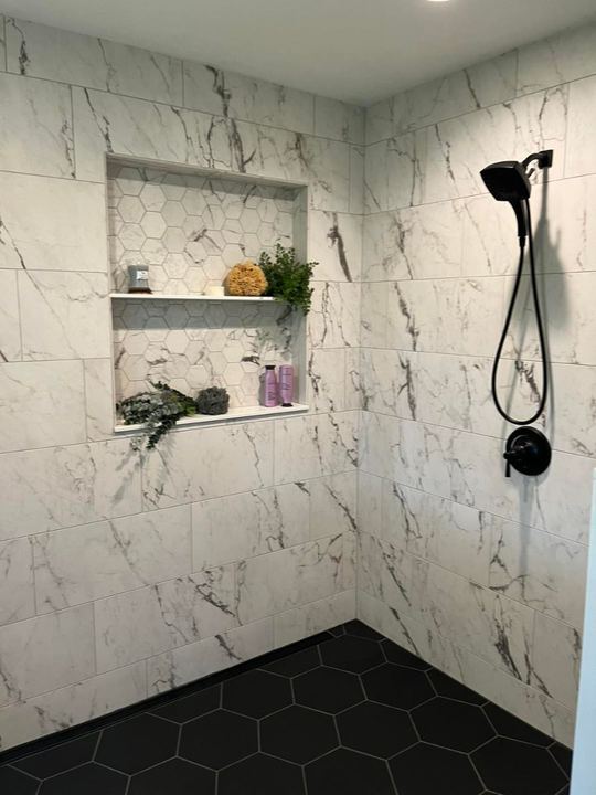 Custom marble-look tile shower with black hexagon floor, shelved niche and matte black fixtures