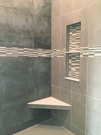 Gray tile master shower with linear glass mosaic accent band, matching niche trim and corner bench