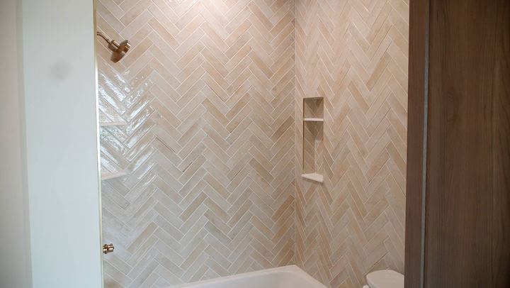 Tub surround with glossy blush herringbone tile, corner shelves, tiled niche and copper fixtures